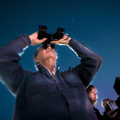 looking through binoculars at the night sky